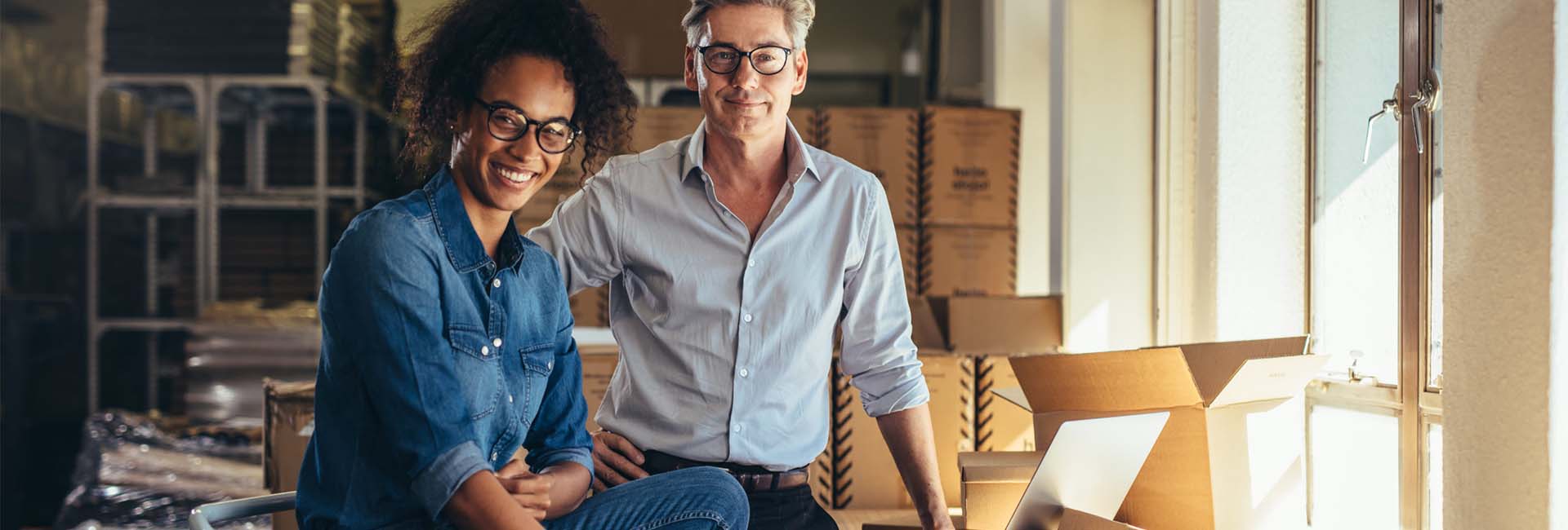 Smiling diverse business owners in a warehouse, showcasing teamwork and entrepreneurship, representing M&F Bank's commitment to supporting small business growth.