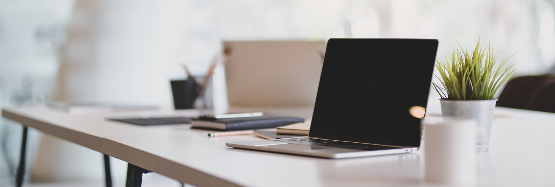 Modern office workspace with a laptop, notebooks, and a potted plant, reflecting M&F Bank's commitment to accessible and personalized banking experiences.