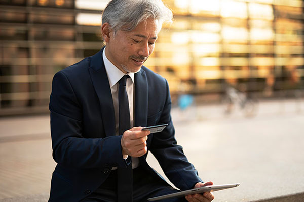 Businessman in a suit using a tablet and holding a credit card, reflecting financial management and business expenses.