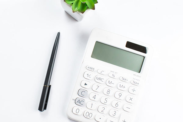 Calculator and pen on a white surface with a small potted plant, symbolizing financial management and business planning for M&F Bank's treasury management services.