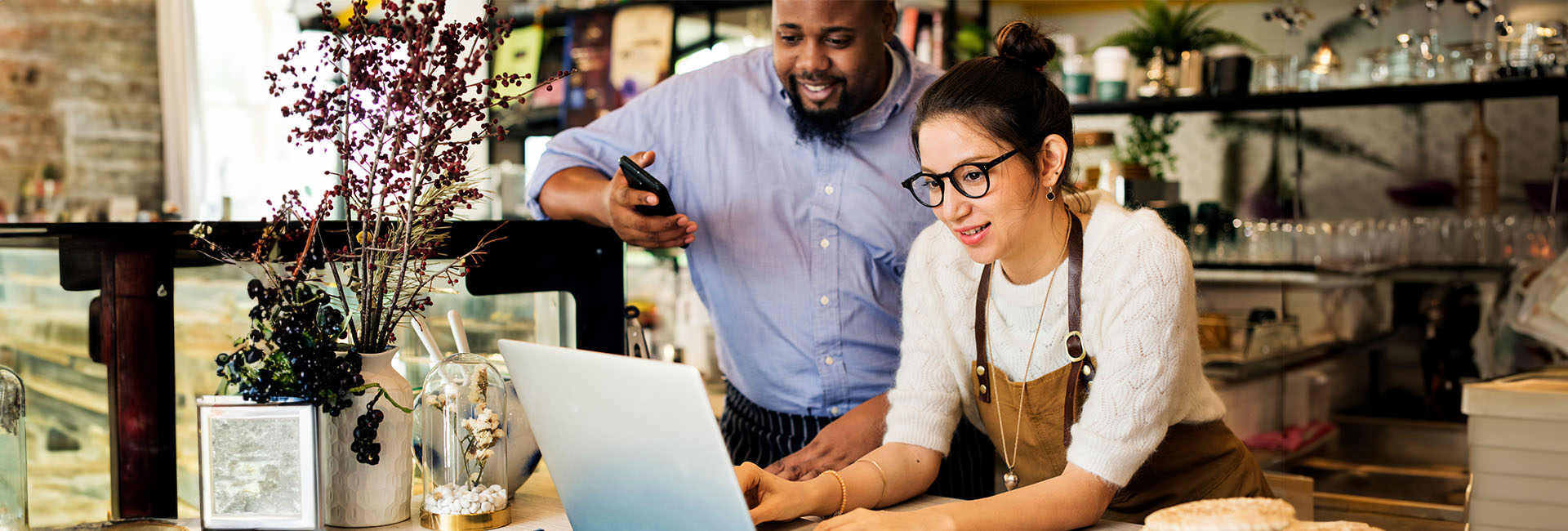 Business Savings header Business owners collaborating at a cafe, using a laptop to manage finances, emphasizing M&F Bank's Business Savings Accounts and financial growth.