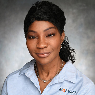 Elaine Johnson, M&F Bank branch manager, wearing a light blue shirt with M&F Bank logo, smiling against a neutral background.