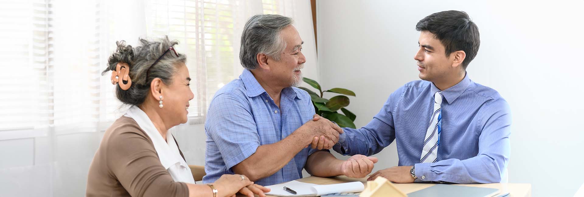 Elderly couple meeting with financial advisor, discussing eldercare financial planning and long-term care options at a table.