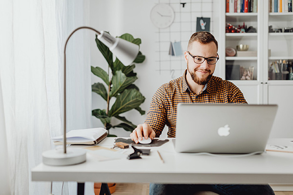Man working on a laptop at a desk with a lamp, notebook, and houseplant, illustrating the digital banking experience at M&F Bank.