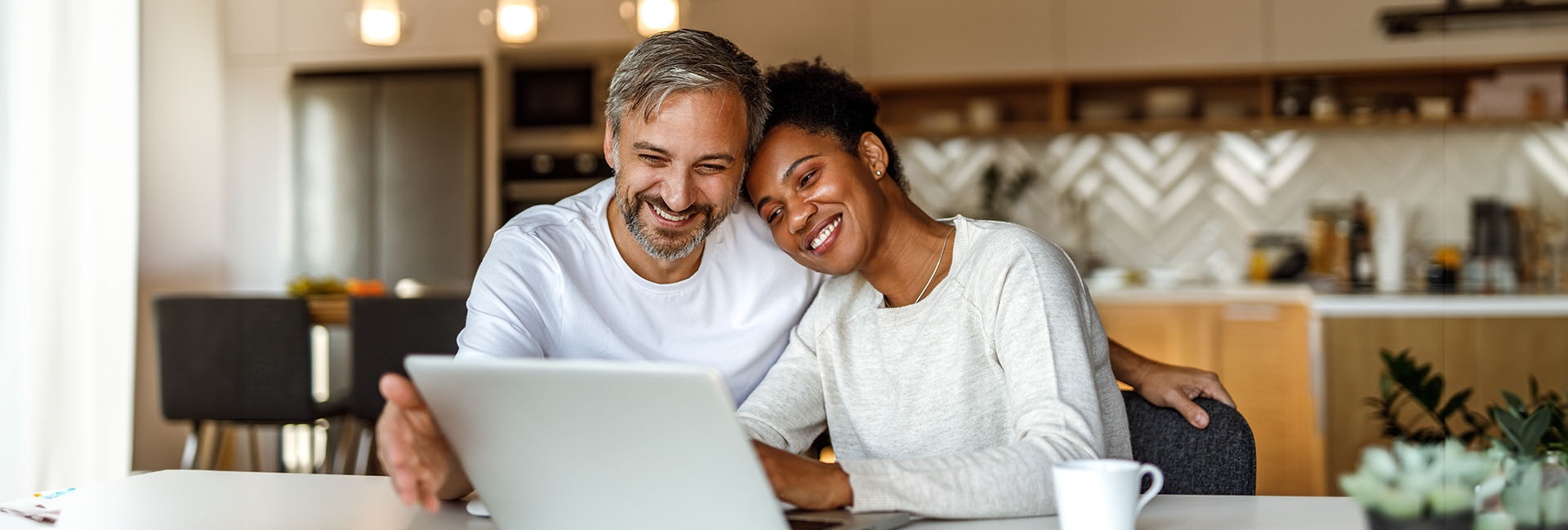 Couple smiling while using a laptop at home, reflecting a positive approach to financial planning and shared goals.