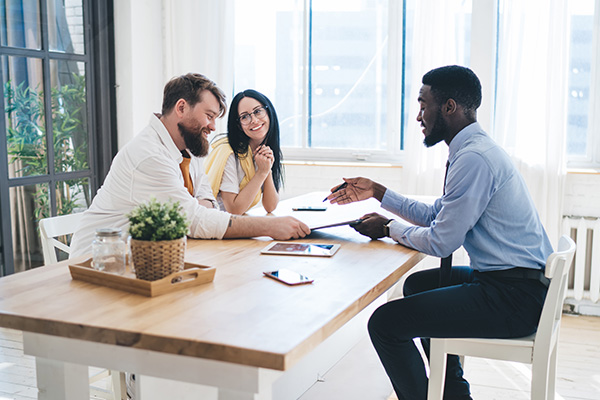 Couple discussing financial options with banker at a table, showcasing personalized banking services and support for loans at M&F Bank.
