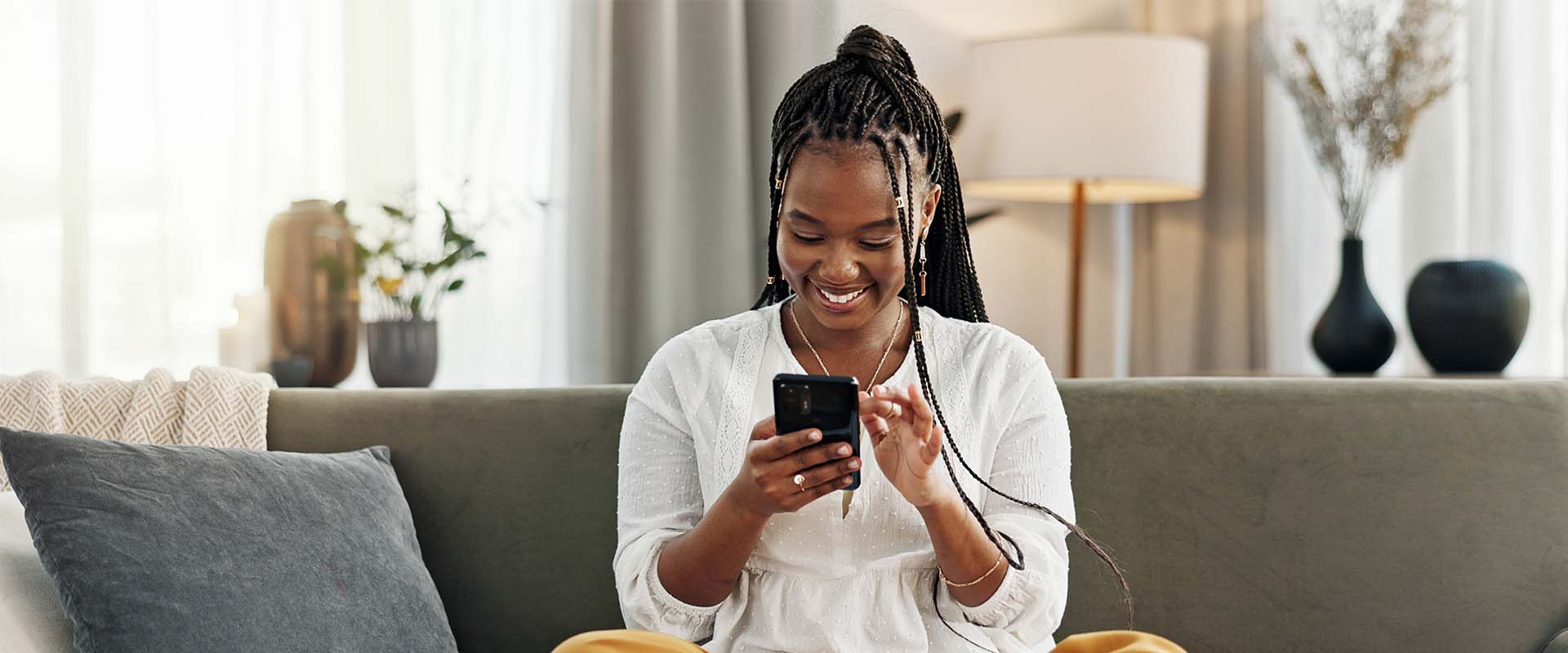 Smiling woman using smartphone to manage finances, showcasing M&F Bank mobile app features in a cozy living room setting.